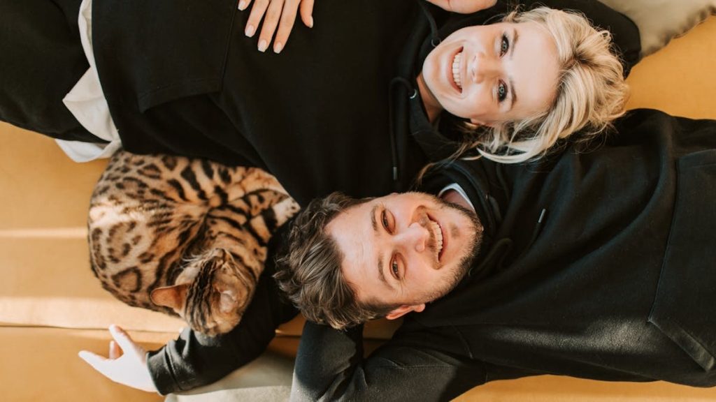 Smiling couple relaxing with Bengal cat indoors, embodying love and comfort.